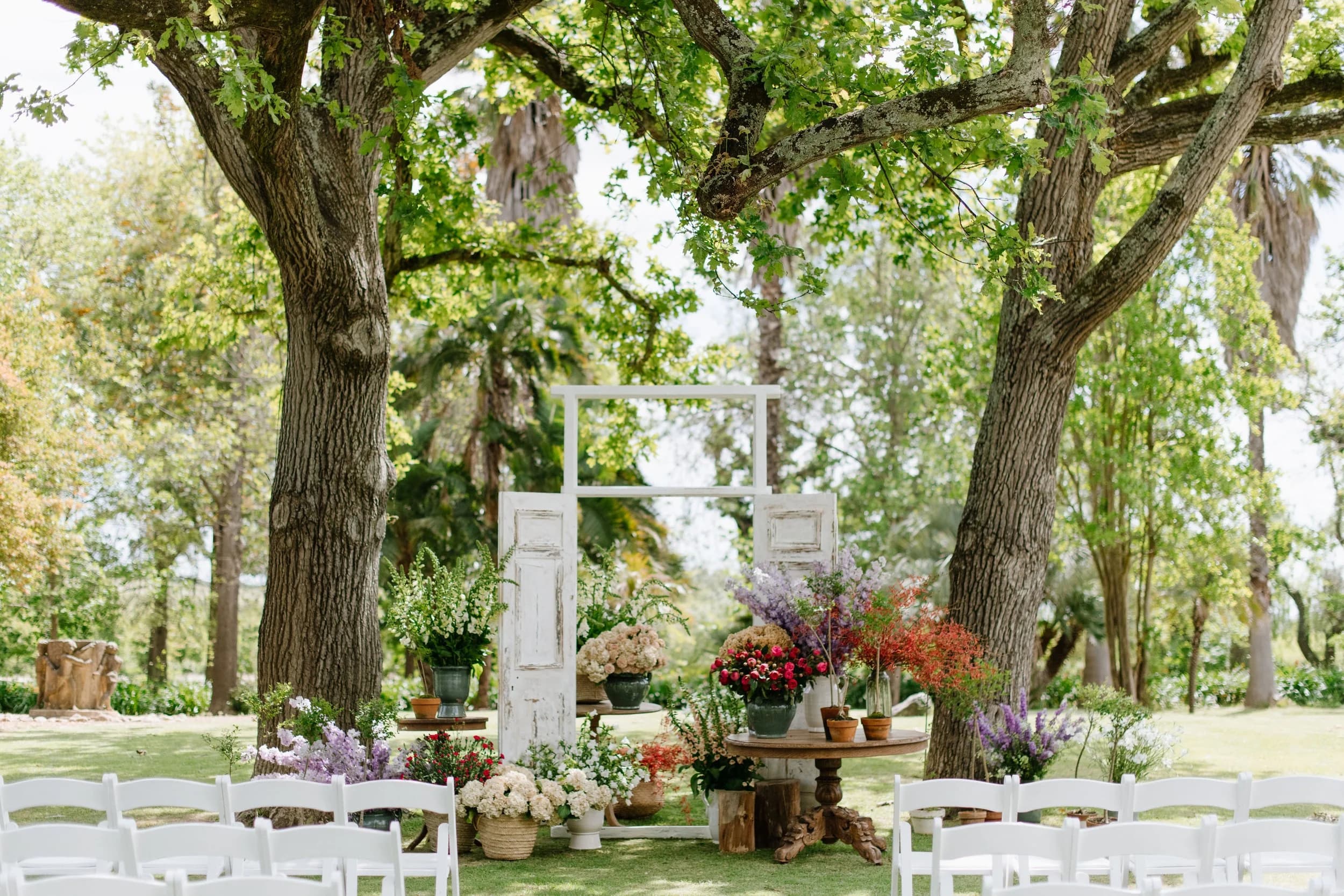 Outdoor ceremony setup at Nooitgedacht Estate, with a whitewashed vintage door arch and floral arrangements beneath ancient oaks